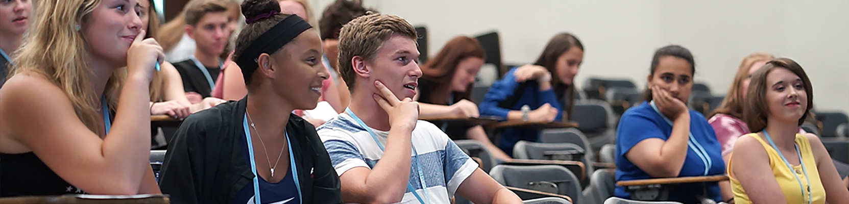 Early College students seated in a lecture hall, listening and smiling during a class session