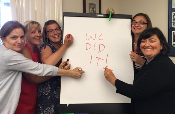Five employees around an easel with a sheet that says "We did it!"