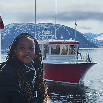 Picture of student giving testimonial, standing in front of a boat