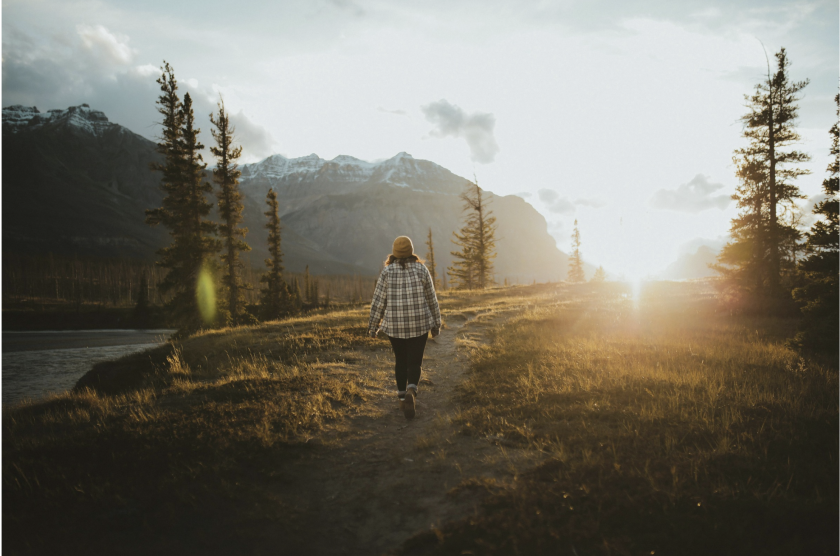 Person walking away from the camera towards a sunrise or sunset in the mountains.