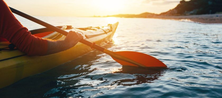 Person kayaking on the water with the sunset in the background.