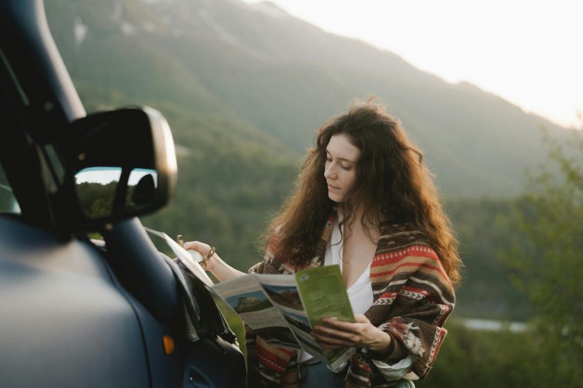 Person holding roadmap outside a parked car.