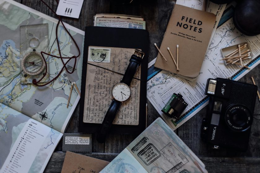 travel items such as matches, maps, watches and cameras scattered on a table.