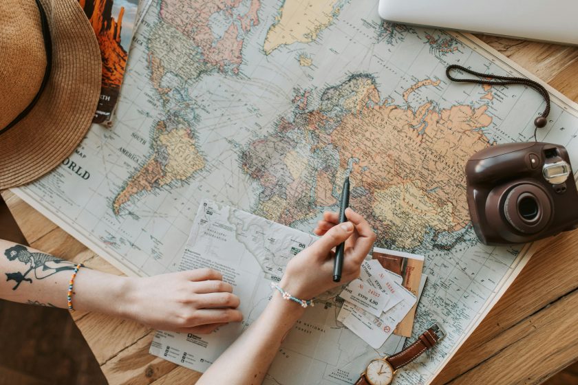 Person looking at world map with a pen, paper, and camera. 