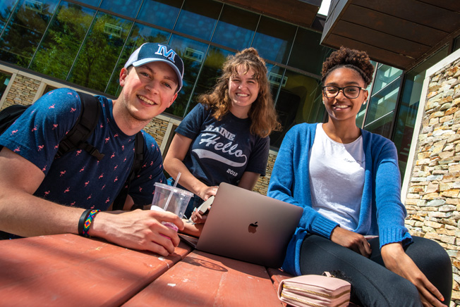 three students with laptop at a picnic table
