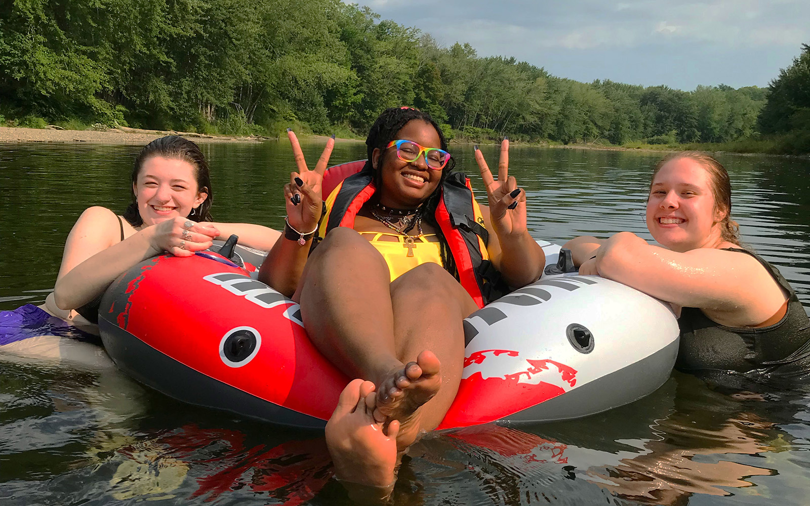 Photo of three female students in a river. Two are swimming and one is sitting on an inner tube floating in the river.