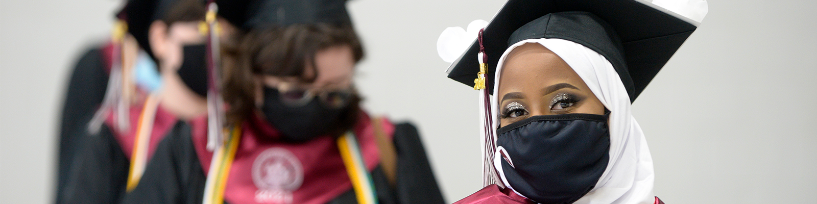 Photograph of a masked, happy graduate with other graduates standing behind them