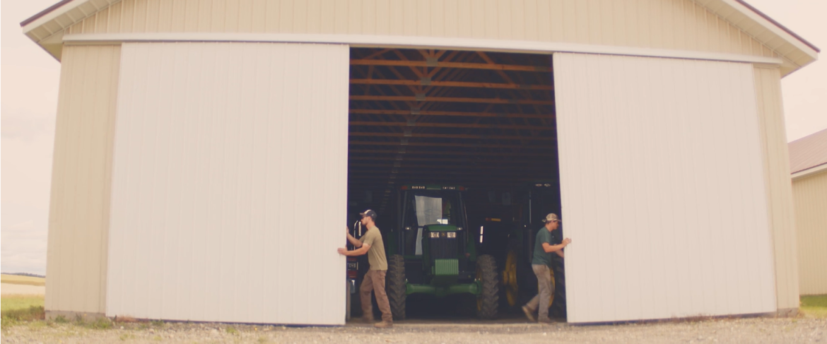Two students opening large sliding barn doors revealing tractor